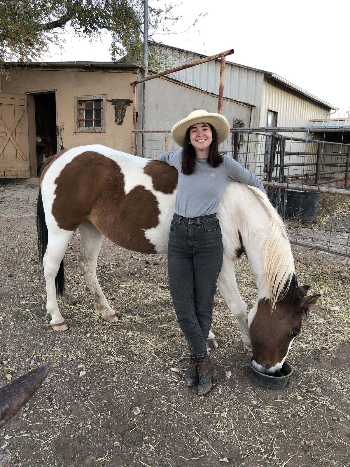 Leigh-Anne in a cowboy hat leaning on a brown-and-white paint horse at a ranch