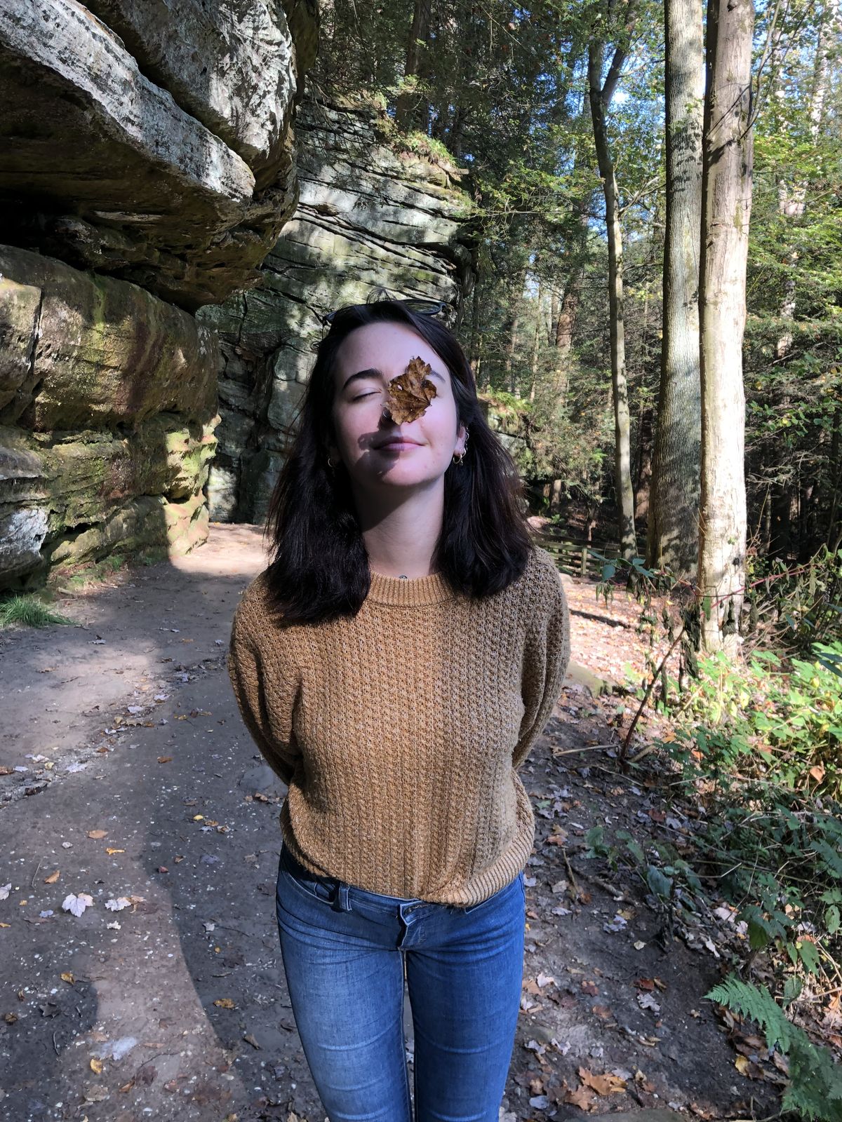 Leigh-Anne on a forest trail with her eyes closed and an autumn leaf stuck to her face